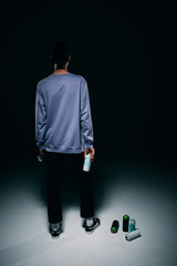 Rear view of street artist with paint cans on dark background