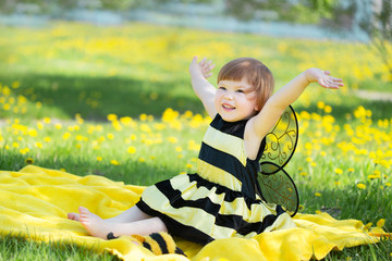 happy little girl in a bee costume walking briskly in a sunny park with dandelions