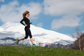 Obraz premium Girl athlete runs in mountains on spring meadow with snow mountains background