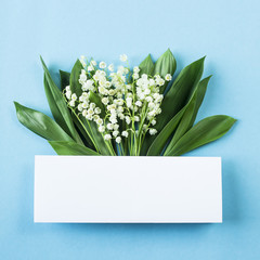 A bouquet of lilies of the valley with a white space for text on a blue background. Top view, flat lay, copy space