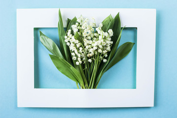 A bouquet of lilies of the valley in a white frame on a blue background. Top view, flat lay