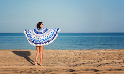 Pretty woman with a mandala round beach tapestry in the ocean coast.