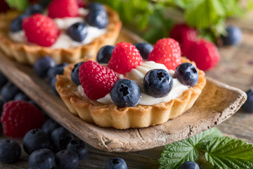  Dessert tarts with raspberries and blueberries on a wooden table.