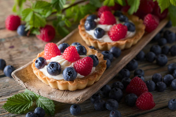  Dessert tarts with raspberries and blueberries on a wooden table.
