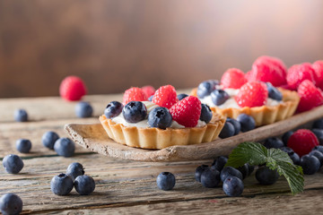  Dessert tarts with raspberries and blueberries on a wooden table.