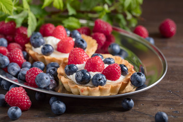  Dessert tarts with raspberries and blueberries on a wooden table.