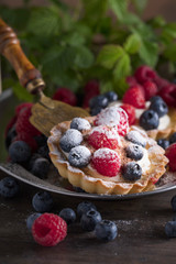  Dessert tarts with raspberries and blueberries on a wooden table.