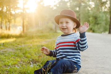 cute boy in hat is sitting in a Park sunset light