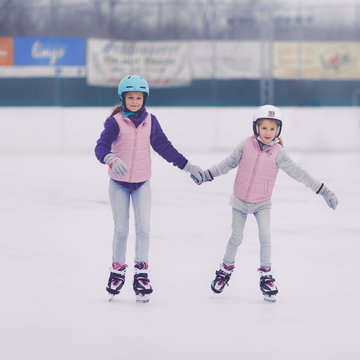 Two Young Smiling Girls Learning To Skate At Ice Skating Ring