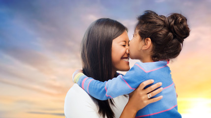 family, motherhood and people concept - happy mother and daughter hugging and kissing over evening sky background