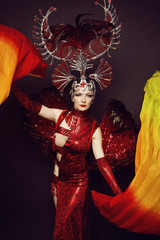 Young model in abstract head decoration, red dress and fans in studio