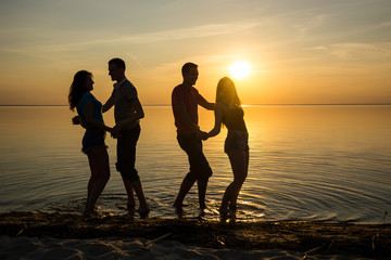 Young people, guys and girls, students are dancing on the beach at sunset background