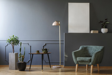 Table between plants and lamp in grey apartment interior with green armchair and mockup