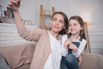 Our plant. Charming cheerful girl sitting on the couch and looking at the tube with her mother