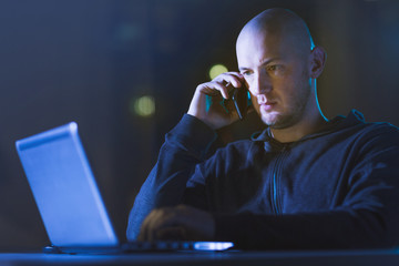 cybercrime, hacking and technology concept - male hacker in dark room networking or using laptop...