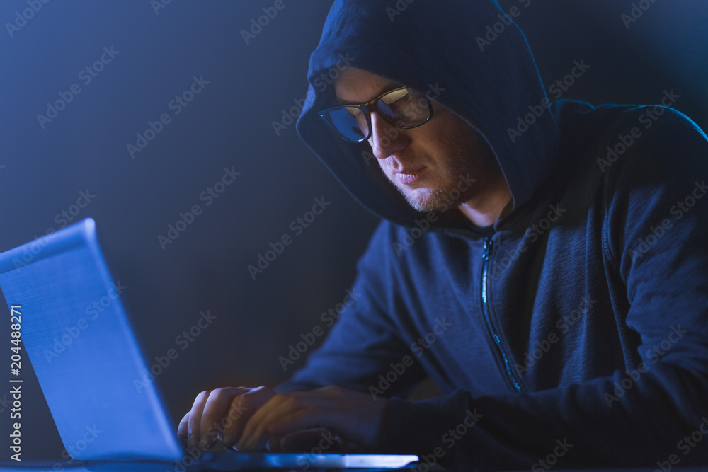 Poster cybercrime, hacking and technology crime - male hacker in dark room using laptop computer for cyber 