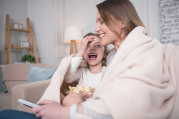 My dear mummy. Young inspired mother sitting with her daughter on the sofa under the blanket and hugging