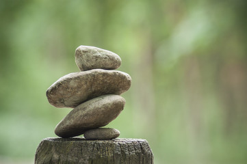 closeup of stones balance on wooden fence on green blurred background