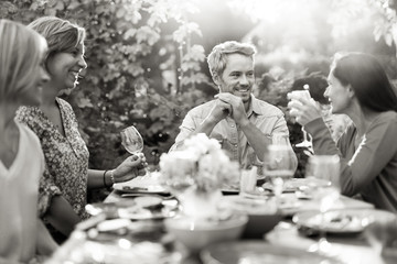 Group of friends gathered around a table in a garden on a summer evening to share a meal and have a...