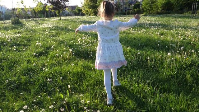 Carefree childhood - little child girl in dress running on summer green meadow grass with blowballs flowers