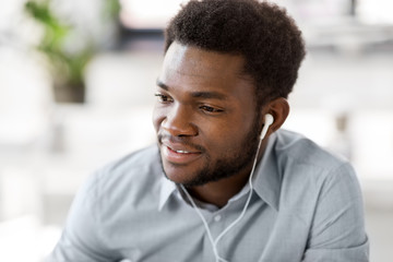 business, technology and people concept - happy african american man with earphones listening to music at office
