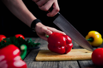 Vegetables getting cut on wooden cutting board. Hand slice pepper with ceramic knife. Food...