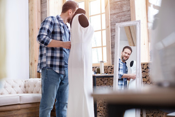 Last touch. Low angle of satisfied male couturier modifying dress while gazing at mirror