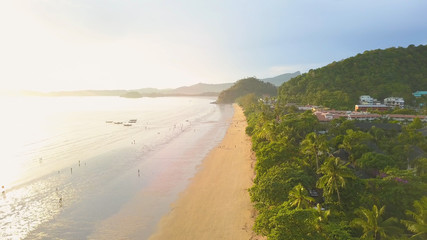 AERIAL: Flying along sandy tropical beach and tourists enjoying their holidays.