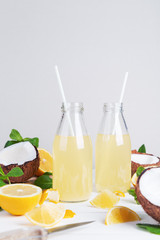 Fresh summer detox cocktail in glass bottles with coconut, lemon and mint on a light background. Space for text.