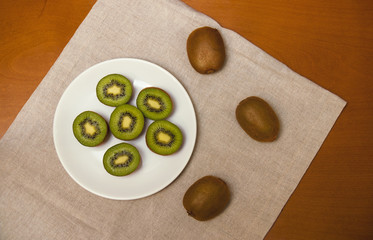 Kiwi fruits on white plate on wooden background. Top view.