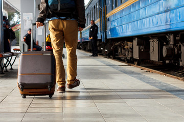 Travel concept. Men wear sneakers shoes and yellow pants travel with brown luggage and backpack on the train station. Sunny day.