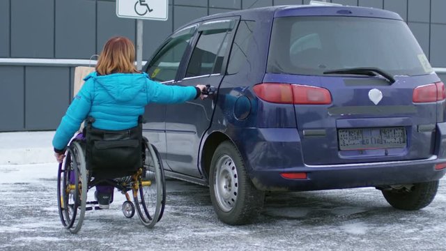 Disabled woman on wheelchair putting bag with groceries on backseat of her car at parking lot