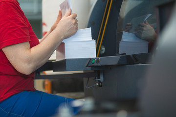 Obraz premium Stack of paper in hands of female worker in front of printing press machine