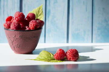 two Raspberries and leaves and more raspberries in a bowl front view