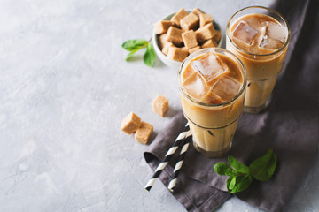 Iced coffee in tall glasses with cream and pieces of sugar, mint and straw