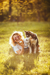 joyful blonde in glasses with ice cream lays on the grass and hugs the husky by her hand in the park in the summer