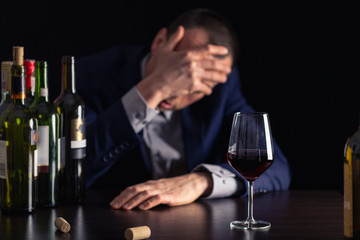 Alcohol abuse by businessman in suit. Silhouette drunk man with glass of wine on first plan.