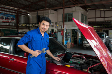 Asian handsome mechanic using laptop computer checking car at garage.