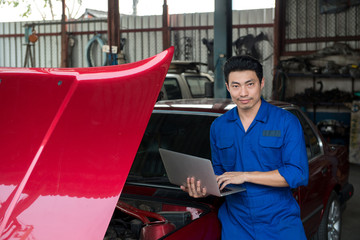 Asian handsome mechanic hold laptop computer checking car at garage.