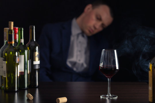 Alcohol abuse by businessman in suit. Silhouette drunk man with glass of wine on first plan.
