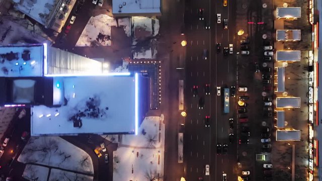 Flying over the roofs of multistory houses and wide streets. Intensive traffic on the street of New Arbat. Neon light on the tops of high buildings. Top-down view at the night city life.