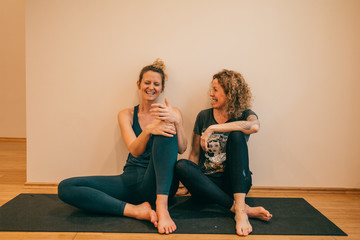 Two positive yoga teachers sitting on the floor laughing