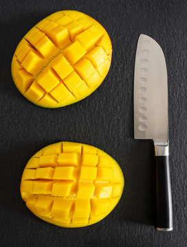 directly above shot of kitchen knife and fresh juicy mango cut in half and diced on slate cutting board