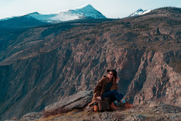 Beautiful young woman with retro backpack on the top of cliff amazing mountain range landscape. Sunset. Hipster. Adventure. Travel lifestyle. Copy space.