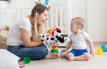 Young smiling woman playing with her little son on floor at bedroom