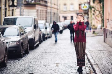 Fototapeta premium smiling girl is standing on wet pavement and closes her eyes with her hands.
