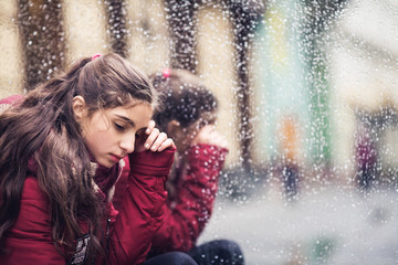 sad girl sits on street near wet mirror in autumn afternoon.