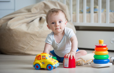 Portrait of adorable baby boy sitting on floor at bedroom and looking in camera