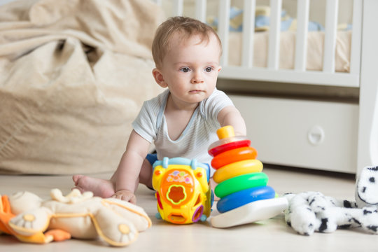 Adorable baby boy playing on floor with colorful toy cars, towers and blocks