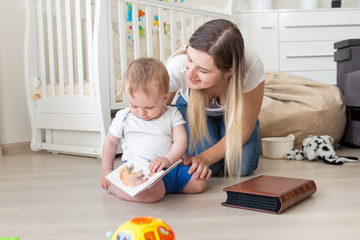 Fototapeta premium 10 months old toddler boy sitting on floor with mother and looking pictures in in book
